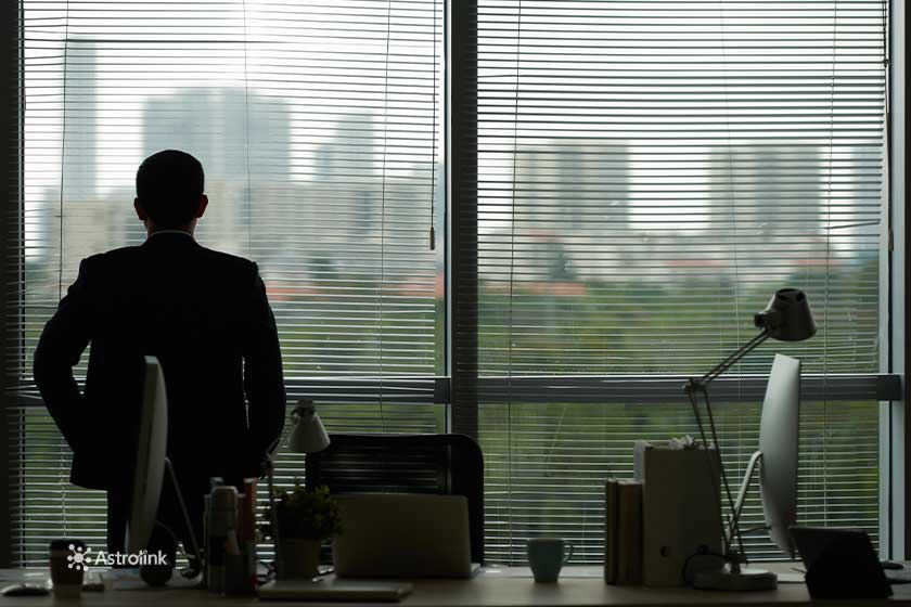 hombre dentro de una oficina de espaldas a la foto, observando un paisaje por la ventana
