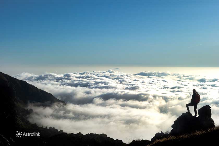 silueta de una persona parada en la cima de una montaña, observando las nubes